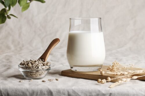 glass of milk on table next to bowl of sunflower seeds with wooden spoon