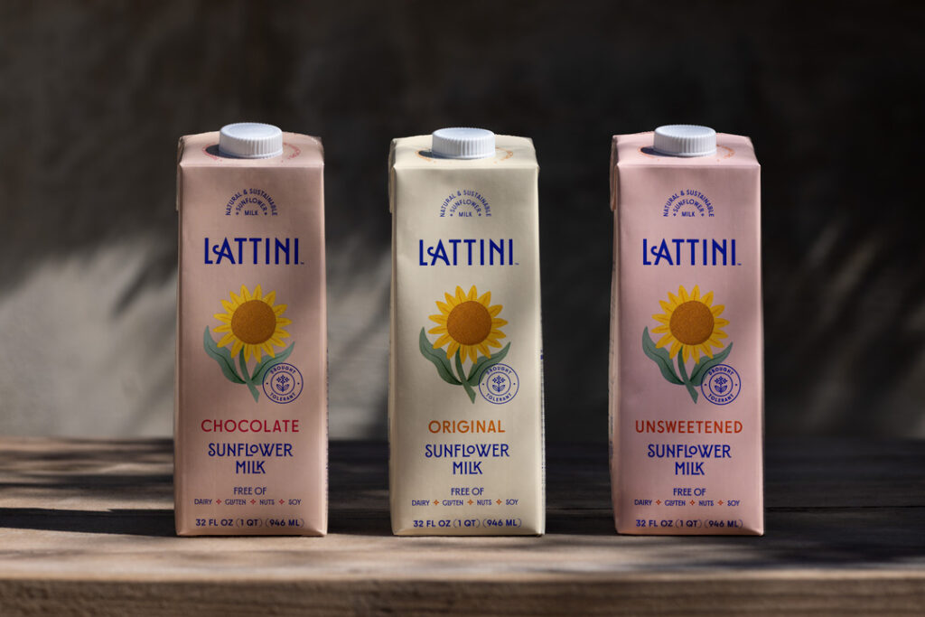 Three cartons of Lattini sunflower milk sit on a wood counter in front of a black background