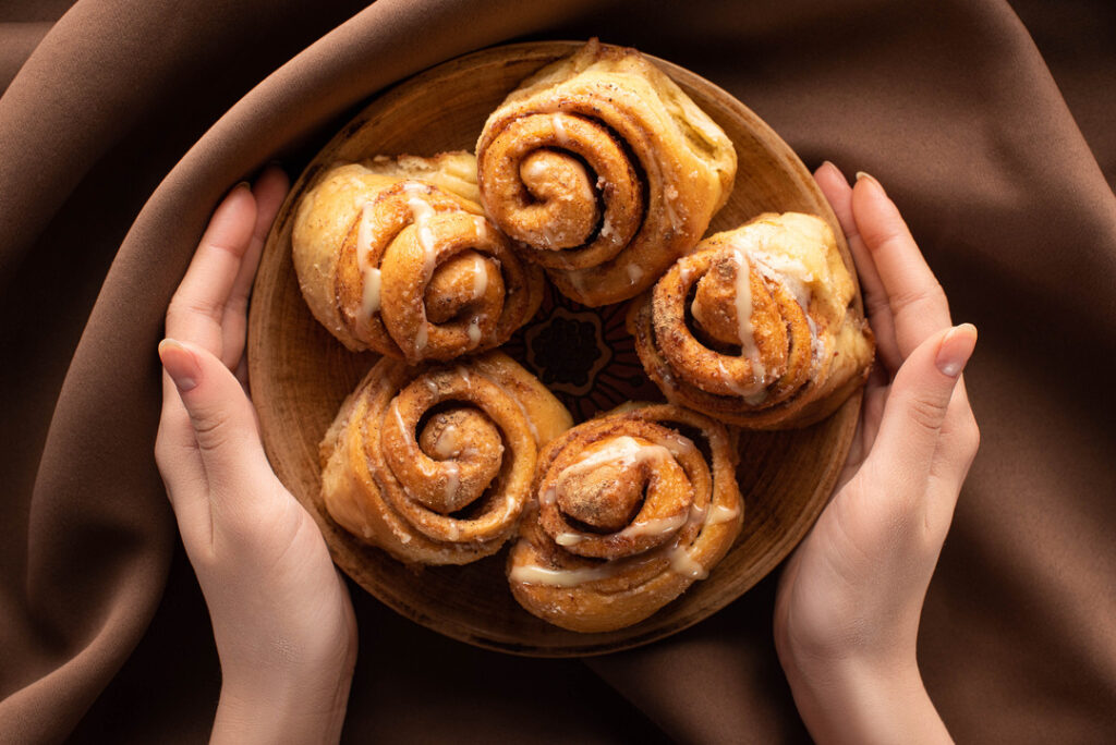 Woman holds bowl of fresh vegan cinnamon rolls in front of a brown cloth